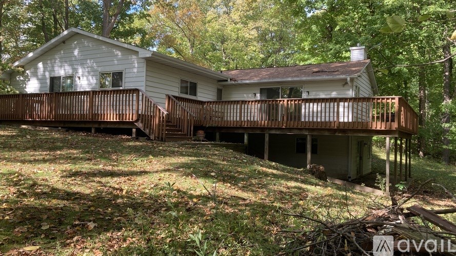 A house with a wooden deck is surrounded by trees.