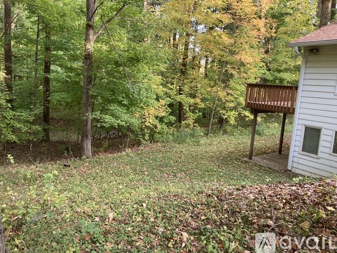 A small white house with a brown deck is surrounded by trees.