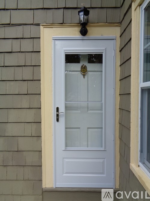 A white door with a glass panel and a brass handle is set in a beige wall.