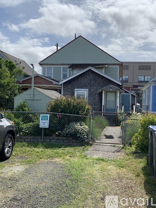A house with a green roof is surrounded by a fence and has a sign in front of it.