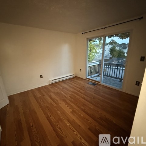 A room with wooden flooring and a sliding glass door leading to a balcony.