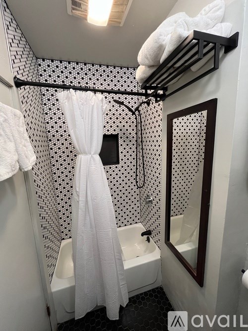 A bathroom with a white shower curtain and a black and white tiled wall.