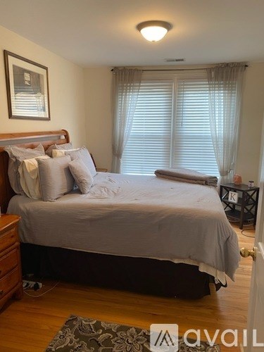 A bedroom with a large bed and a window with white curtains.