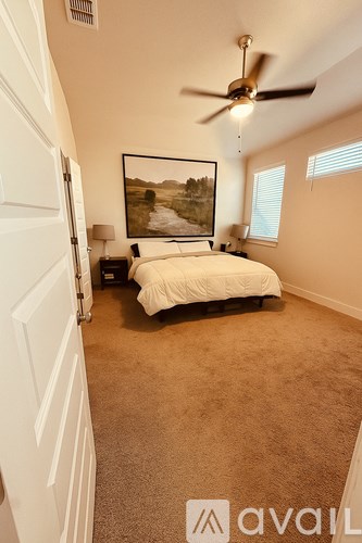 A bedroom with a bed, a ceiling fan, and a painting on the wall.