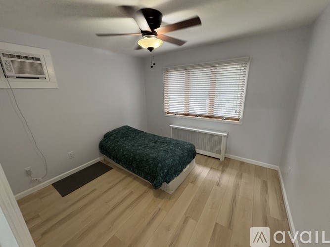 A room with a bed, a ceiling fan, and a window with blinds.