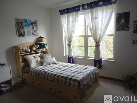 A bedroom with a bed, a window with curtains, and pictures on the wall.