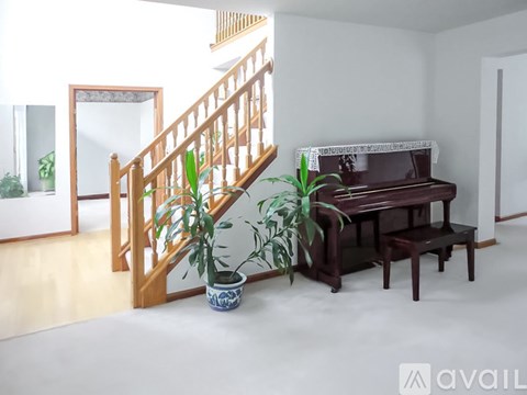 A brown piano with a white top sits in a room with a wooden staircase.