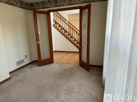 A room with a carpeted floor and a wooden staircase.