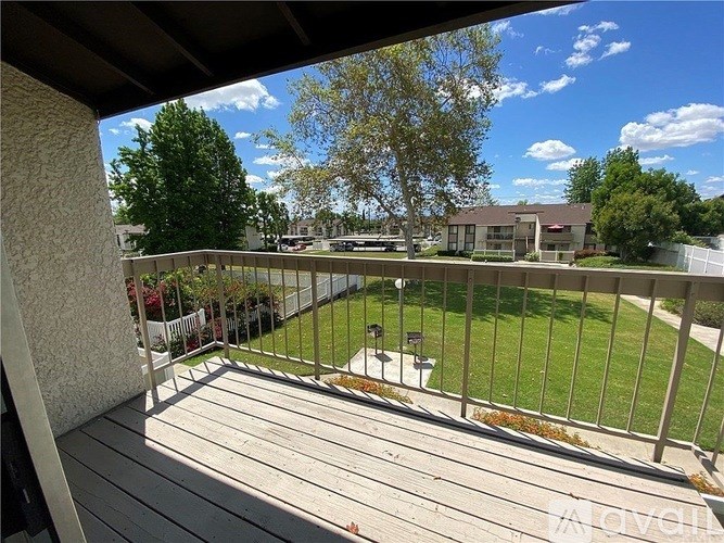 A balcony with a wooden floor and a metal railing overlooking a green lawn and trees.
