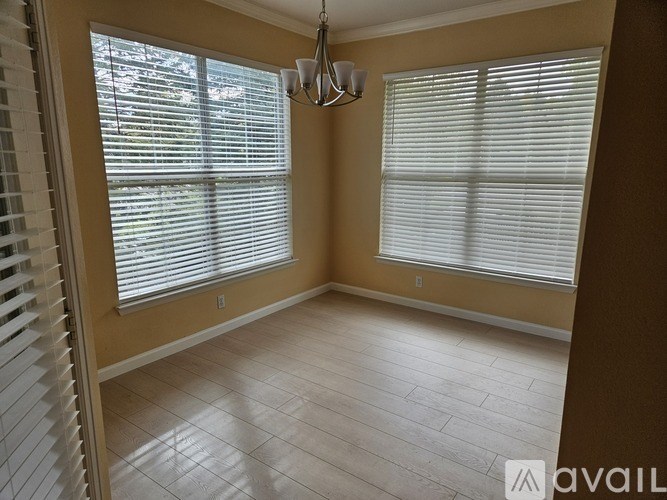 A room with a window covered in blinds and a chandelier hanging from the ceiling.