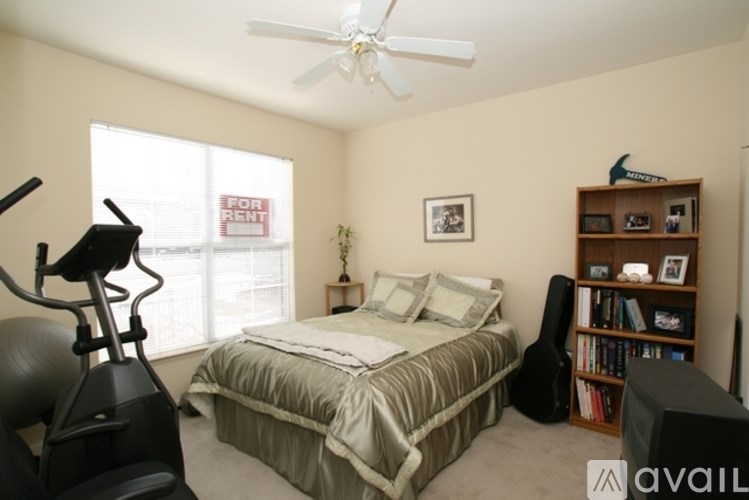 A bedroom with a bed, a fan, a bookshelf, and a treadmill.