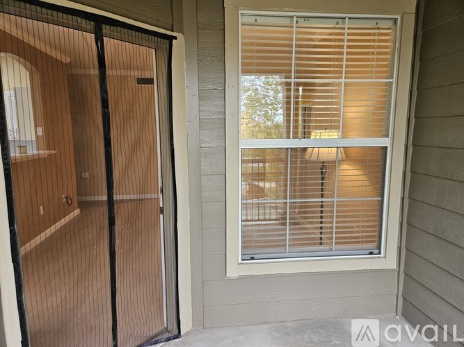 A glass door with a black frame is open to a room with a window covered in white blinds.