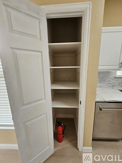 A white door is open to a pantry with a red fire extinguisher on the floor.