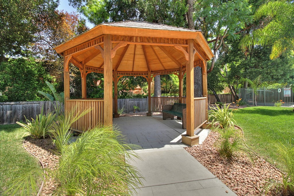 A wooden gazebo with a concrete walkway in front of it.