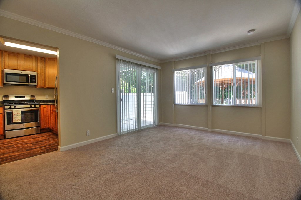 A spacious living room with a kitchen area to the left and sliding glass doors to the right.
