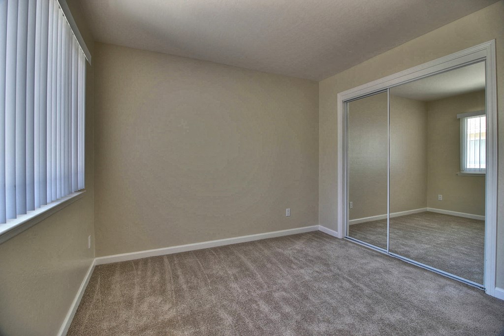 an empty bedroom with a mirrored closet and carpet