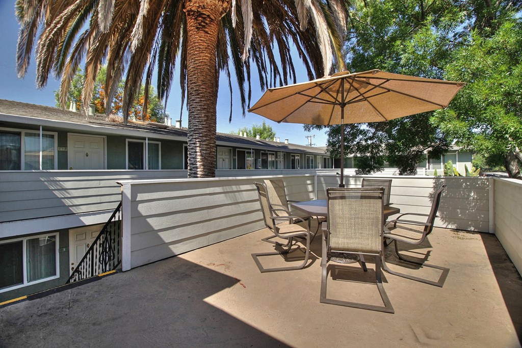 A patio with a table and chairs under an umbrella with a palm tree in the background.