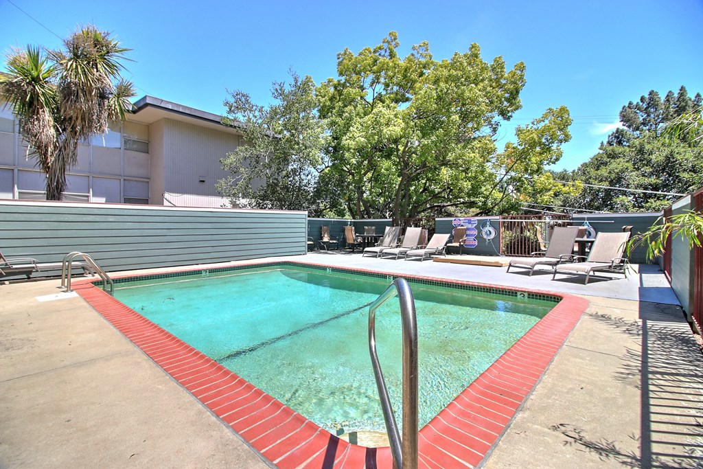 a resort style pool with lounge chairs and a building in the background