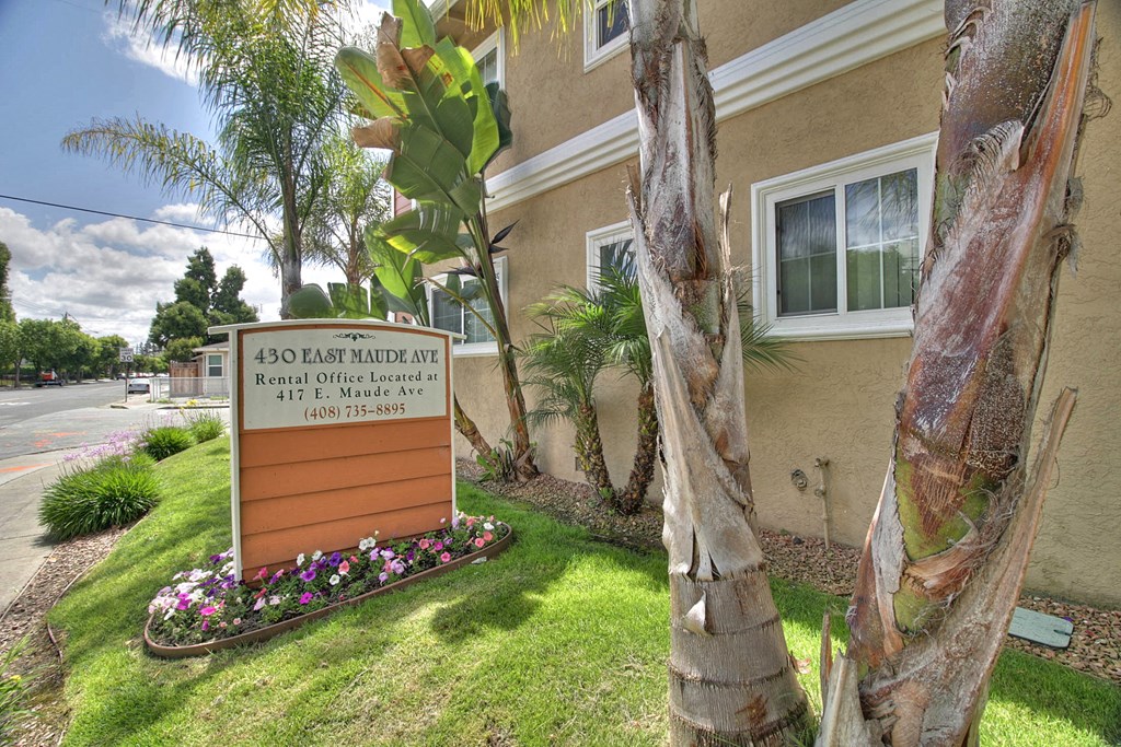 a sign in front of a building with trees and flowers