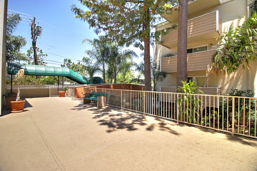 A green slide is in the middle of a concrete courtyard.