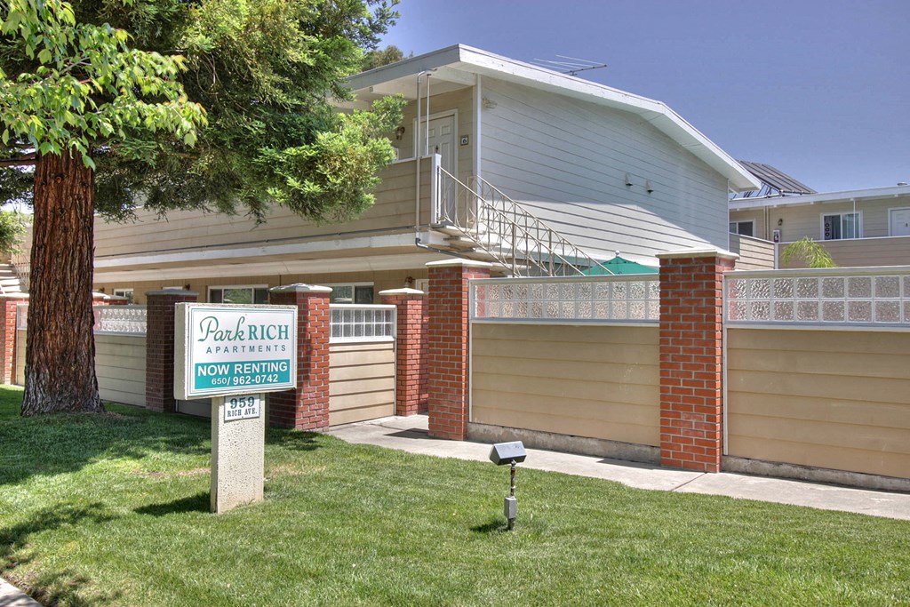 A sign for Park Rich Apartments is in front of a two-story building.