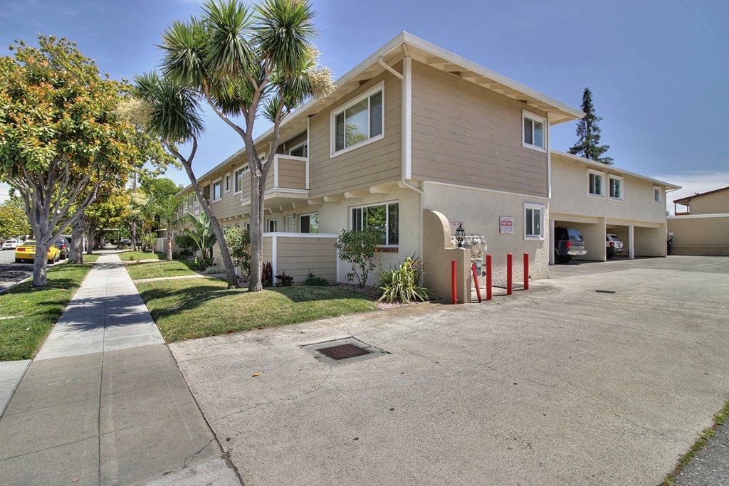 a beige house with a sidewalk and palm trees