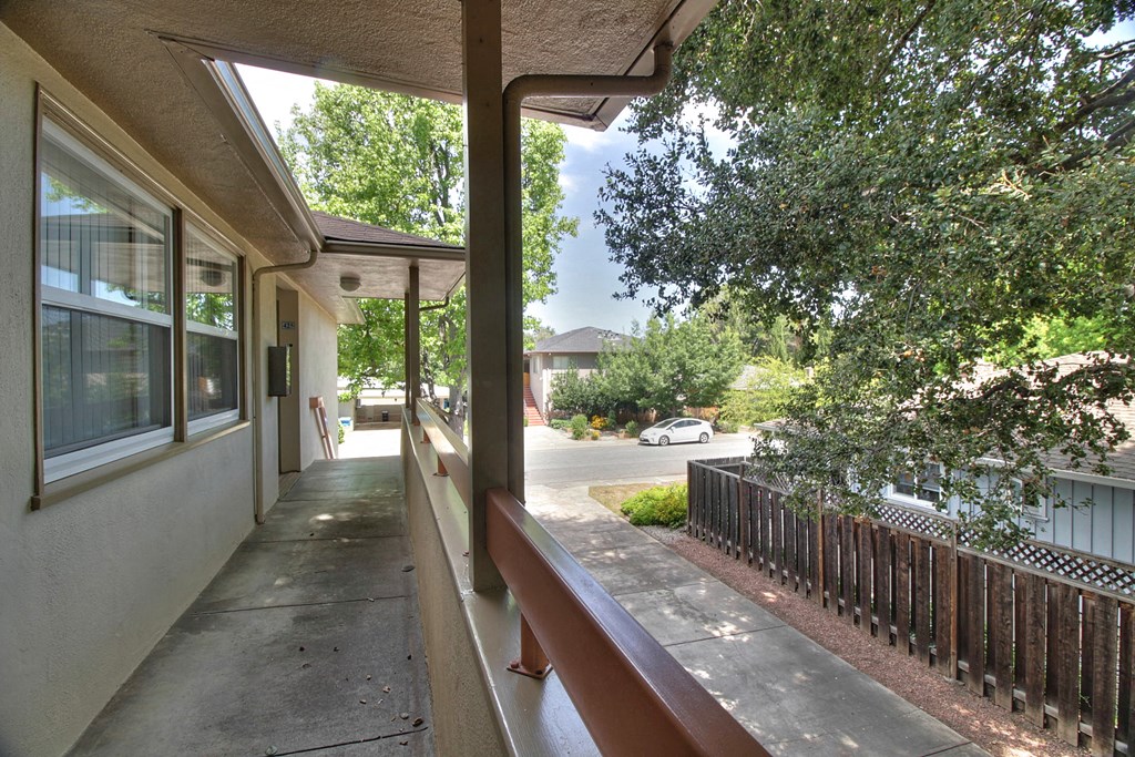 the view from the porch of a building with a sidewalk and trees
