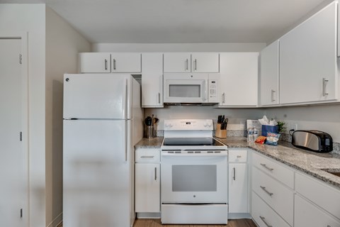 A white kitchen with a refrigerator, microwave, oven, and toaster.
