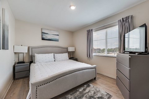 A bedroom with a large bed, a dresser, and a window with blinds.