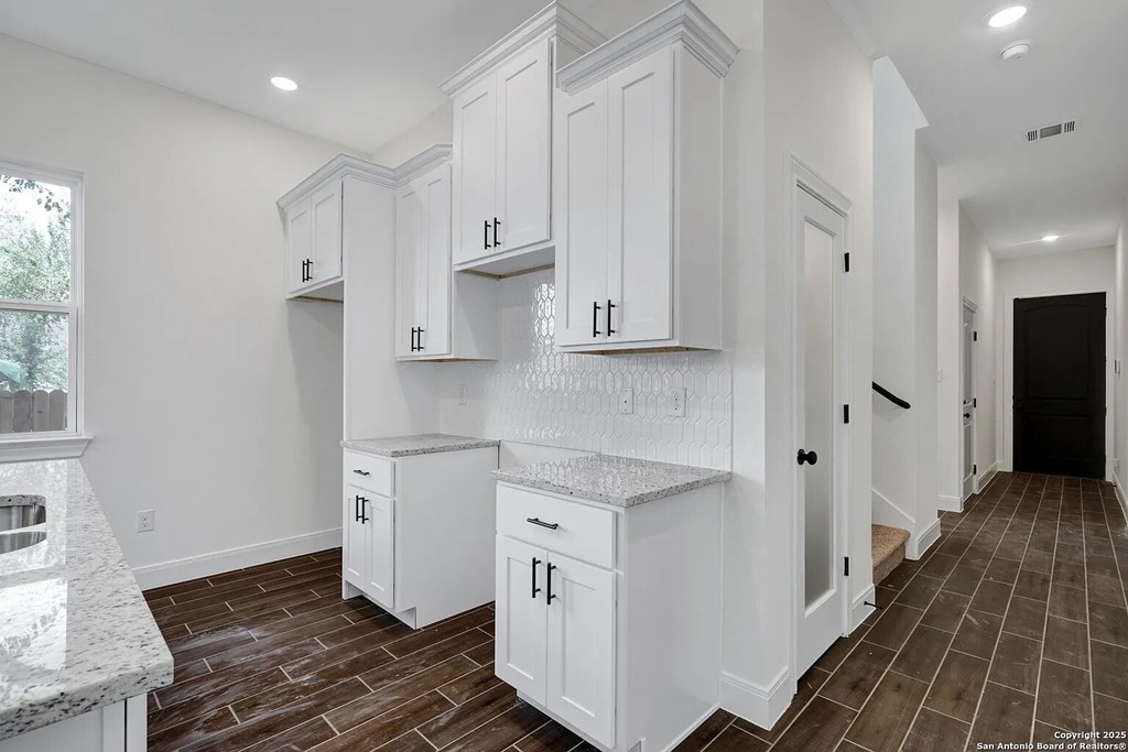 A kitchen with white cabinets and brown floors.