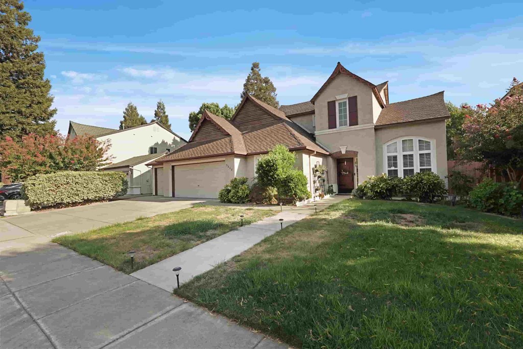 A house with a brown roof and white trim is surrounded by a well-manicured lawn and trees.