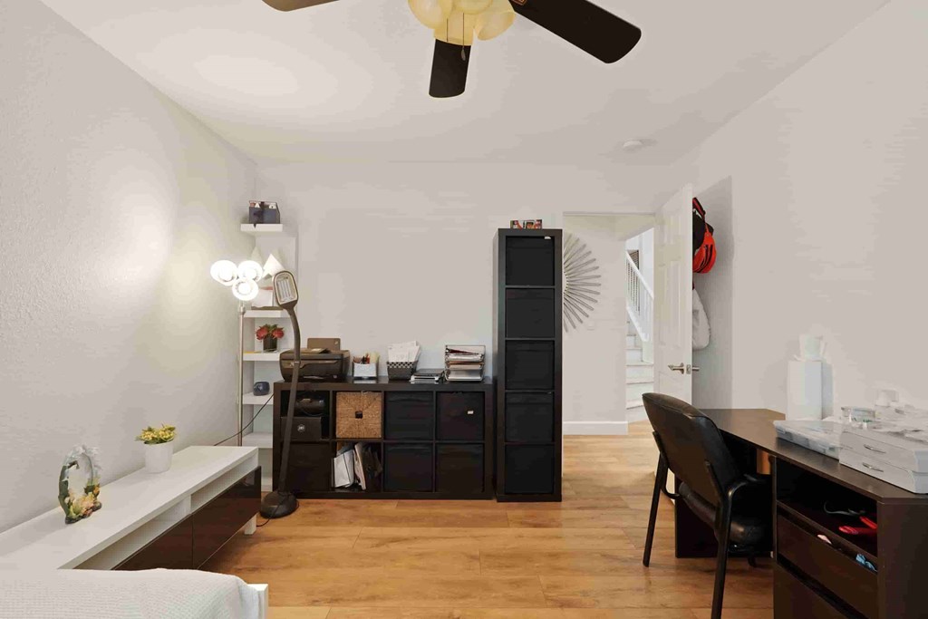 A room with a ceiling fan, a desk, and a chair.