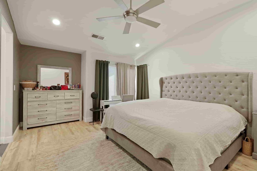A bedroom with a large bed, a dresser, and a ceiling fan.
