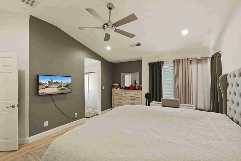 A bedroom with a large bed, a flat screen TV, and a ceiling fan.