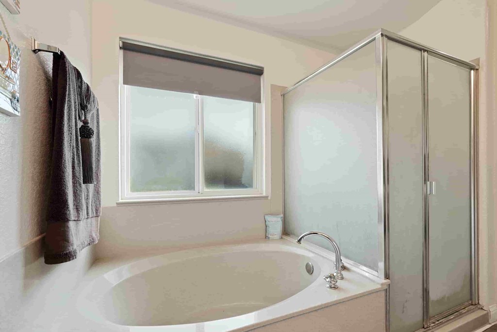 A bathroom with a tub, shower, and a window.