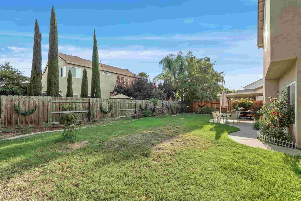 A backyard with a fence, trees, and a house.