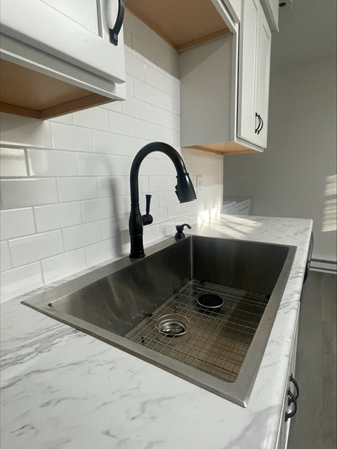 A kitchen sink with a black faucet and a white countertop.