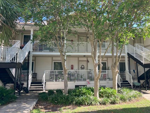 A white building with a balcony and trees in front.
