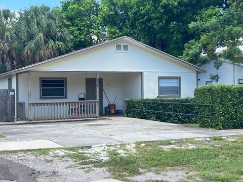 A white house with a porch and a hedge in front.