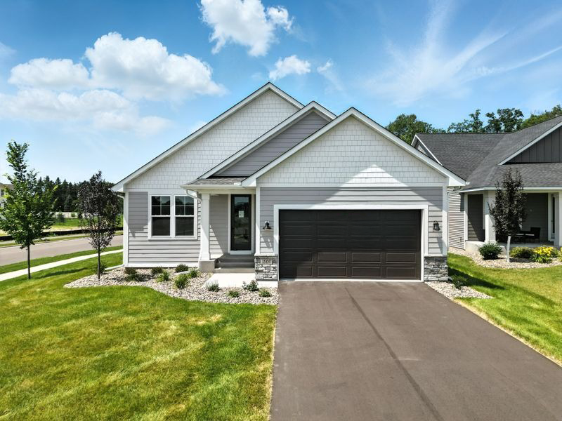 A house with a grey garage door is surrounded by a grassy lawn.