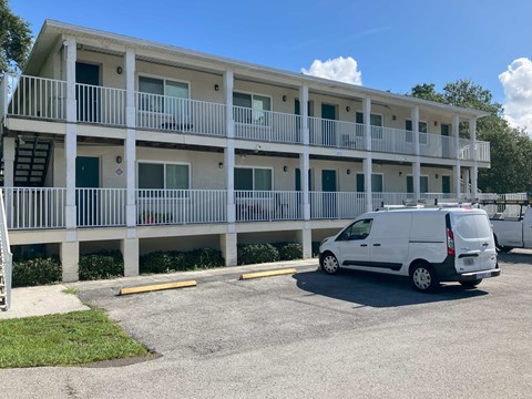 A white van is parked in a parking lot in front of a white building with balconies.