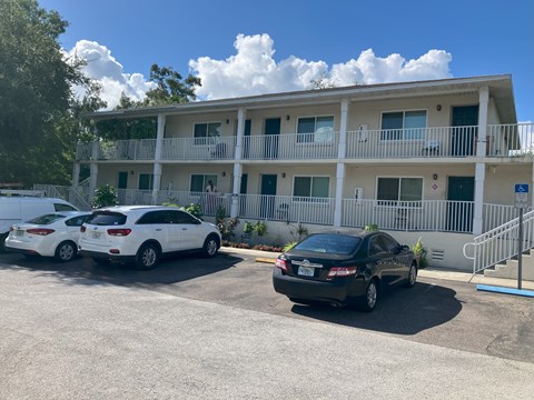 A black car is parked in front of a white building with a balcony.