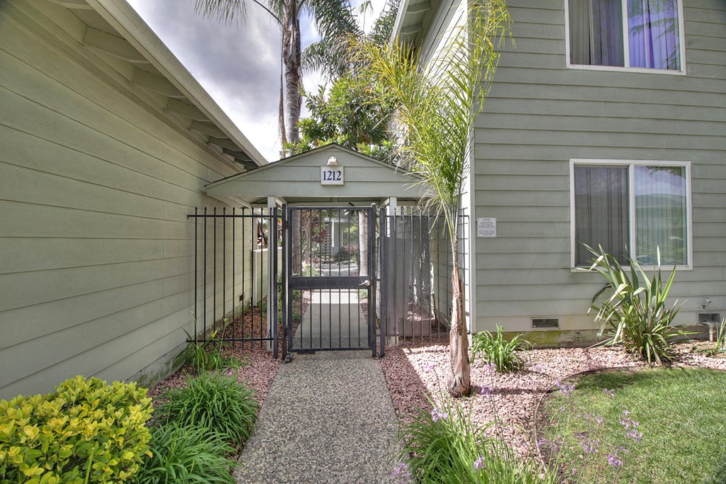 the entrance to a house with a gate and a yard with a path and plants