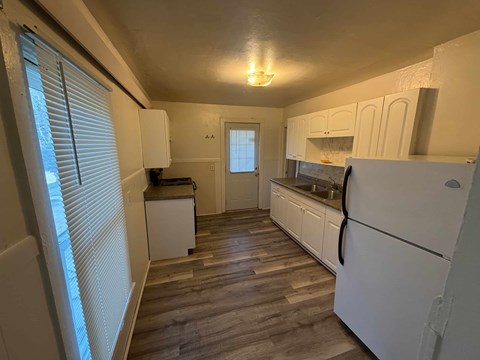 A kitchen with white appliances and wooden floors.