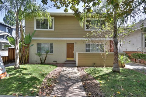 the front of a yellow house with a sidewalk and grass