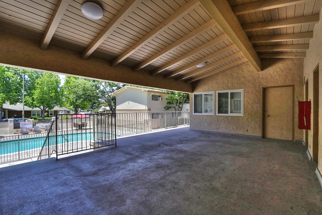 A covered patio area with a pool and a fence.