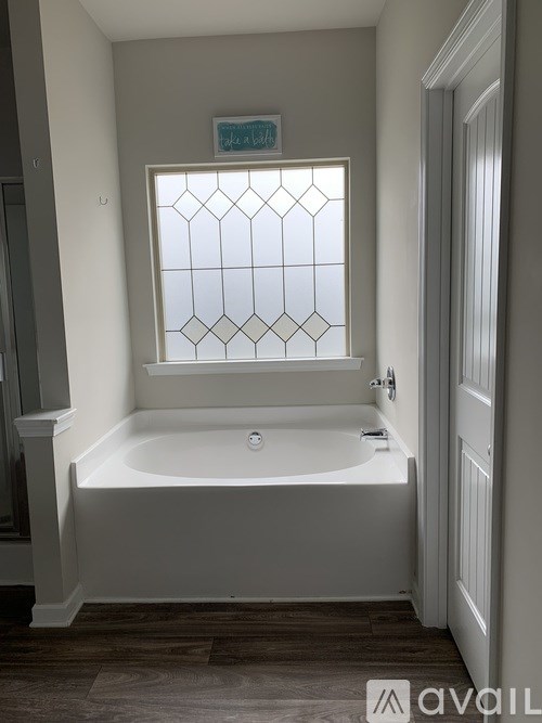 A white bathtub sits under a window in a bathroom.