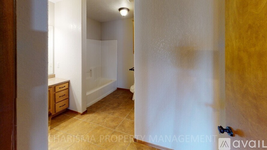 A room with a wooden floor and a white wall with a doorway leading to another room.
