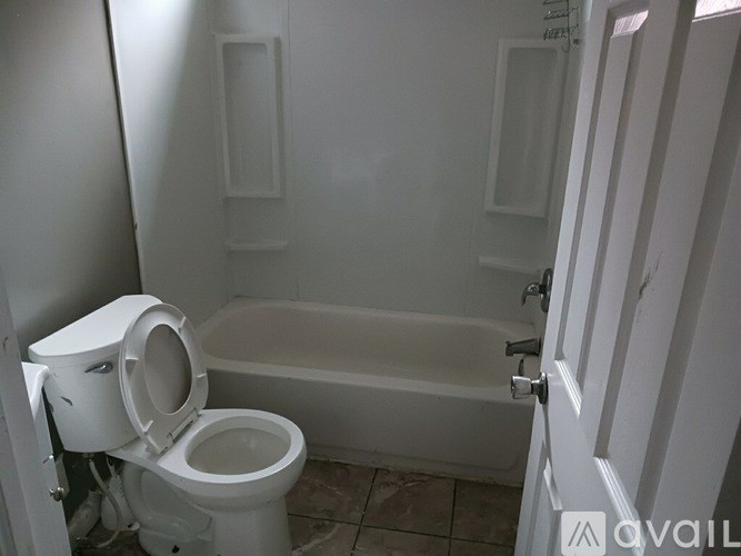 A white toilet is in a small bathroom with a bathtub.