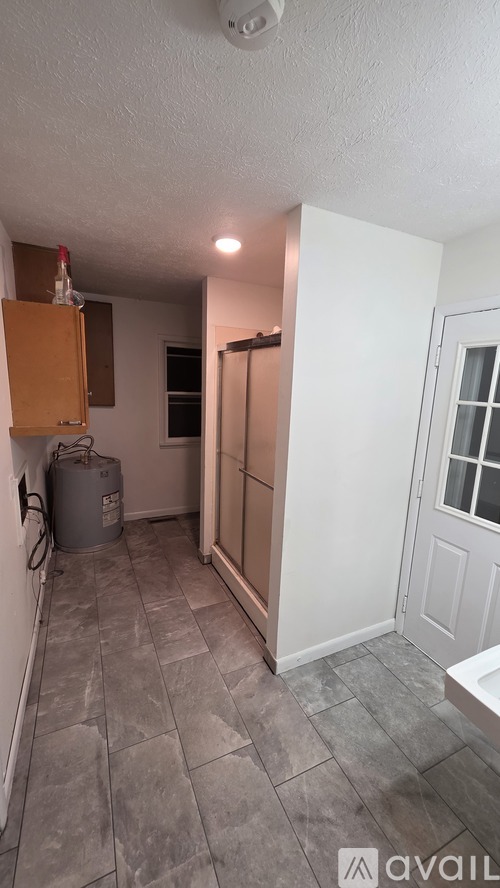 A kitchen area with a refrigerator, a trash can, and a door leading to another room.